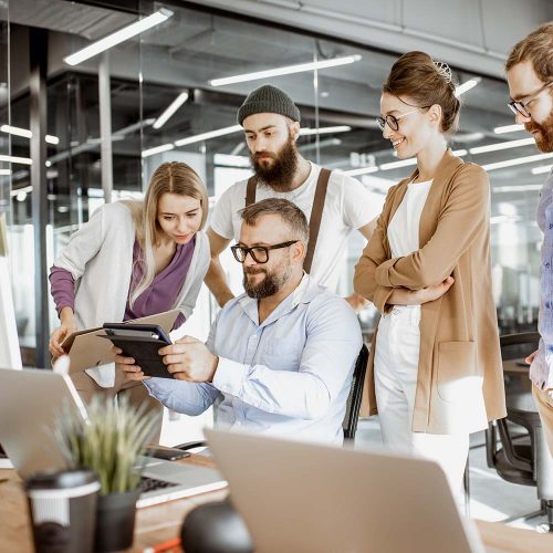 Senior manager having a meeting with office workers standing together near the working place in the modern office. Concept of a small conference and teamwork